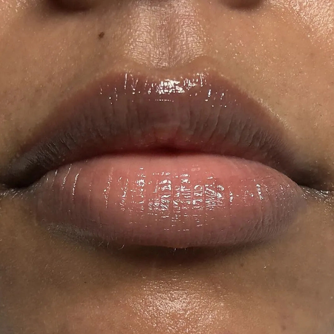 Close-up of a person's lips wearing a glossy, sheer pink lip product with a high-shine finish.