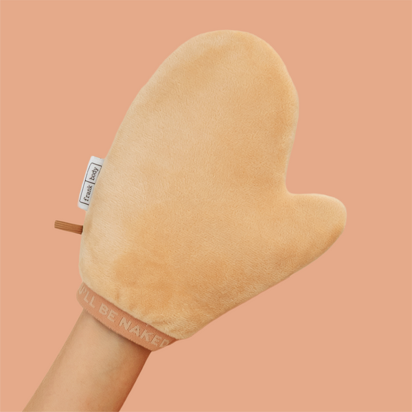 A hand wearing the frank body Double Trouble Tanning Mitt on a tan background.