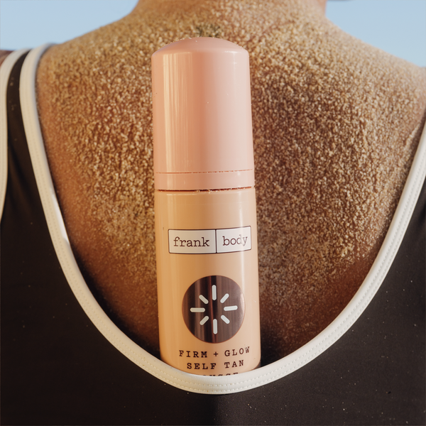 A bottle of frank body Firm + Glow Self Tan Mousse held against a tanned back.