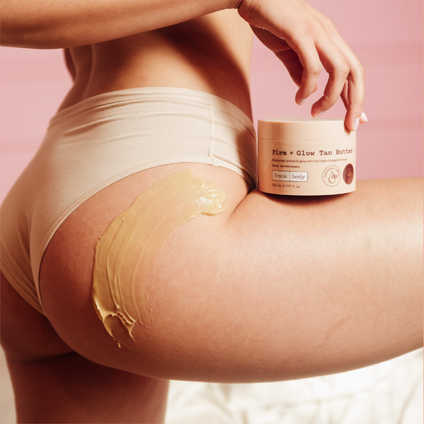 A woman in cream underwear holding a jar of frank body Firm + Glow Tan Butter with the butter smoothed over her hip.