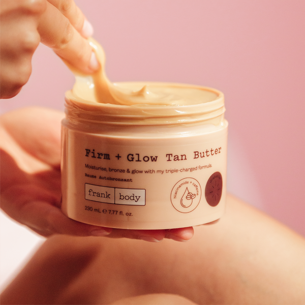 A hand scooping frank body Firm + Glow Tan Butter from its open jar.