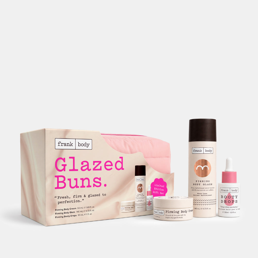 Frank Body Glazed Buns set featuring a pink and beige gift box, a large smoothing body butter bottle, a smaller body butter jar, a serum bottle, and a dropper bottle, arranged on a light gray background.