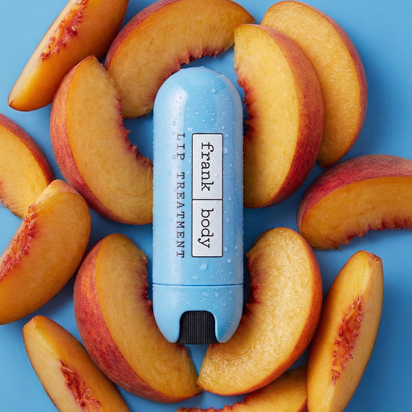 Blue lip balm with 'frank body' branding surrounded by sliced peaches on a blue background