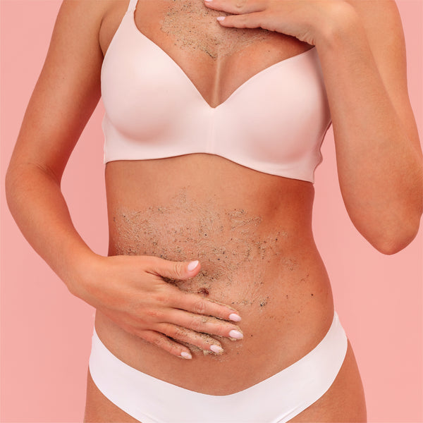 A close-up of a woman's torso wearing a pale pink bra and white underwear, with dry, flaky skin peeling across her chest and stomach, set against a solid pink background.